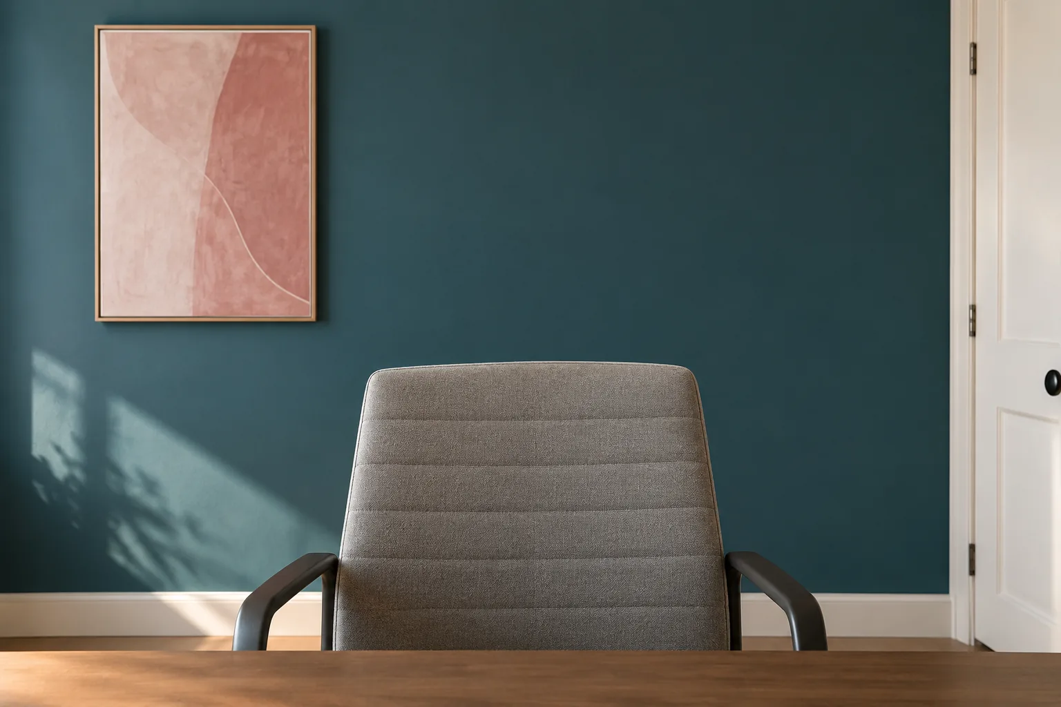 A simple petrol wall behind an empty office chair with one small rose artwork.